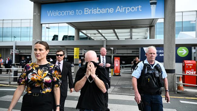 Mr Lees covered his face from waiting media as he was escorted by detectives out of the terminal. Picture: Dan Peled / NewsWire