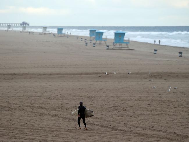 A surfer walks on the beach in Huntington Beach, California. Picture: Getty