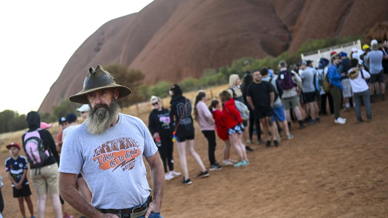 A man wearing a T-shirt saying 'I chose not to climb' stands next to tourists lining up to climb Uluru. Picture: Lukas Coch/AAP