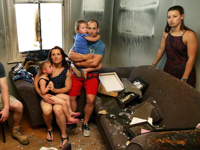 Joel and Angela Hudson with children Lilli, 4, and Grace, 3, and Isabelle Devetak in the burnt out ruins of their house after a repaired Samsung washing machine caught fire. Picture: Peter Lorimer