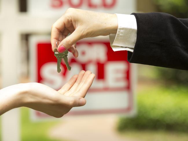 iStock photo of agent handing over keys in front of a for sale / sold sign. For On the Pulse column in Cairns Post weekend real estate liftout.