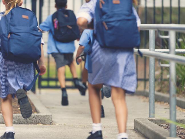 School children running away. They are wearing uniforms and carrying backpacks. They are having a race. Multi ethnic group with Asian, Caucasian and Aboriginal children. Rear view