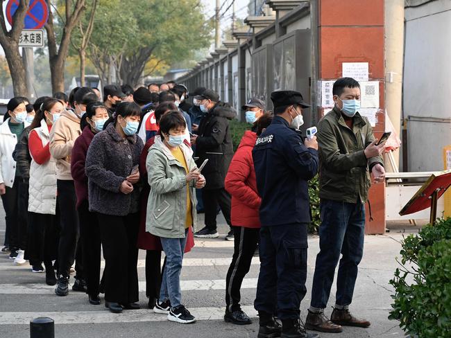 People wait in line to receive Covid-19 coronavirus vaccination booster shots as a security guard checks body temperature of a man along a street in Beijing. Picture: AFP