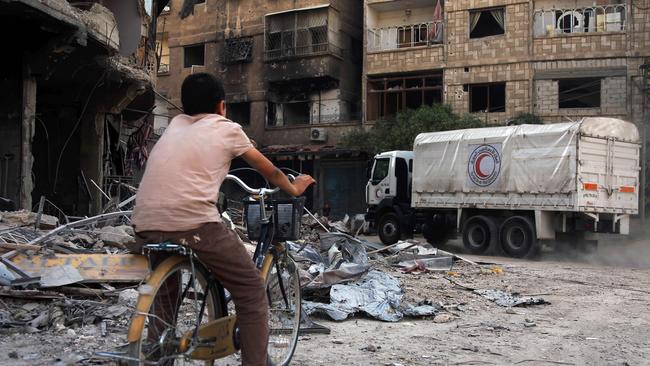 A Syrian boy rides his bike behind a Syrian Arab Red Crescent truck delivering aid on the northeastern outskirts of the capital Damascus. Picture: AP