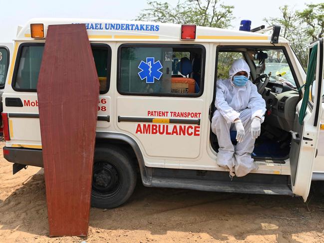 This picture taken on May 8, 2021 shows a Michael Undertakers and Ambulance Services employee, seen wearing personal protective equipment (PPE) suits, resting by his vehicle during the burial of a Covid-19 coronavirus victim at a Christian cemetery in Pali village near Faridabad. - As India grapples with a mounting coronavirus death toll, new services ranging from specialist funeral firms, Bollywood film set cleaners and low-budget deliverymen are easing the pain and making a living. (Photo by Sajjad HUSSAIN / AFP) / TO GO WITH INDIA-HEALTH-VIRUS-ECONOMY-STARTUPS,FOCUS BY NIVRITA GANGULY