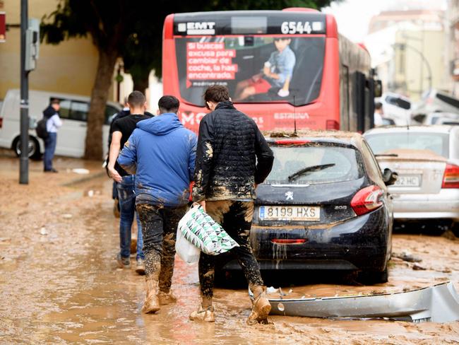 Residents walk next to piled up cars following floods in Valencia’s De La Torre area. Picture: AFP