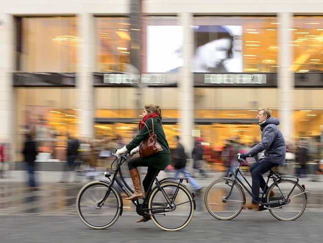 Antwerpen, Belgium - March 1, 2014: Two cyclists passing in front of the fashion shopping centre at dusk time. Bicycles are widely used transportation vehicles in Antwerpen. Bar Burbure, Antwerp. Travel story GCB