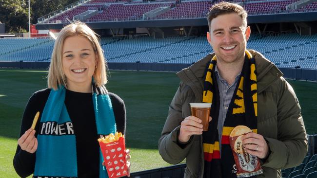 Port fan Alice McKeough and Crows supporter Lachlan McLeod pictured with some of the Oval’s current food offerings. Picture: Supplied