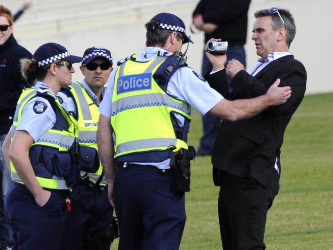 Protester Elio Celotto is escorted off the Sandown course by police.