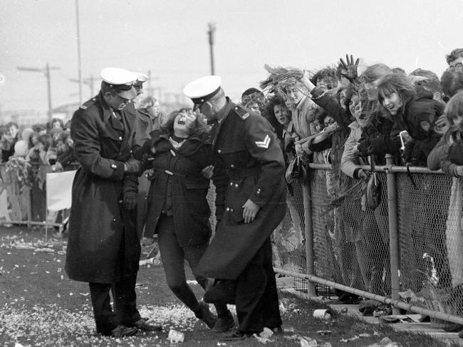 1964: Police help a young woman as crowds gather at Essendon Airport to greet The Beatles on their visit to Melbourne. File picture