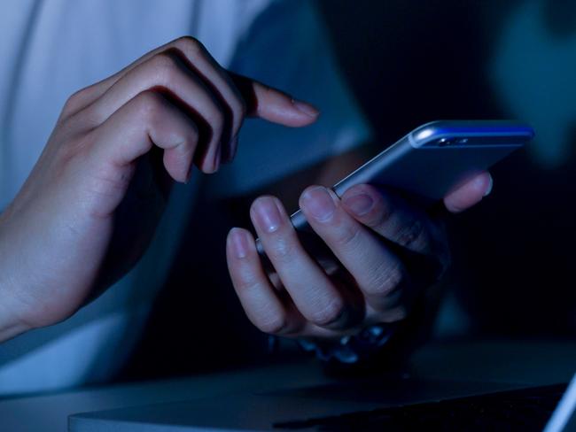 close up young man hand holding smartphone for access by unlock on screen and using laptop for register website on internet in the late night , internet addiction concept