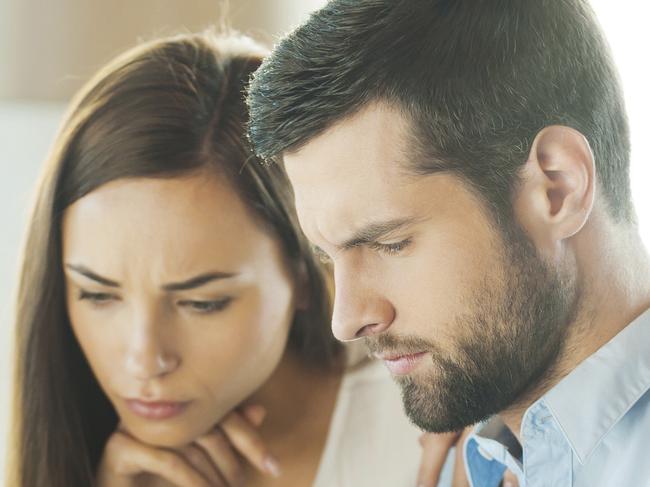 Concentrated young man holding documents and looking at them while woman sitting close to him and holding hand on chin