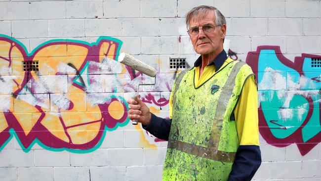 Pride of Australia nominee John Oakey pulls out his pot of paint and brushes over the graffiti. Picture: Carmela Roche