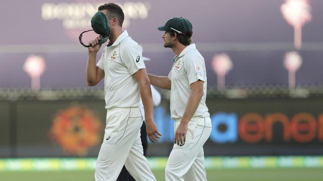 A devastated Josh Hazlewood covers his face with his baggy green as he is consoled by Joe Burns after injuring a hamstring. Picture: AP