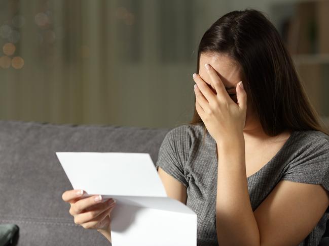 Sad woman reading a letter in the dark at home, renter, tenant, eviction, bill, stress, anxiety - for Herald Sun realestate