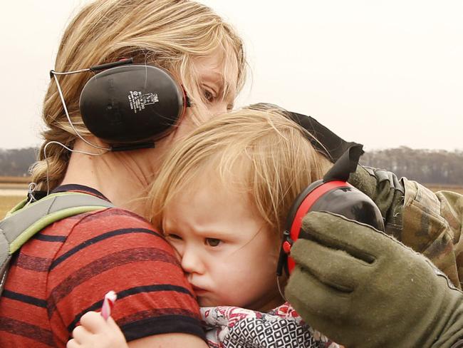 Mallacoota fires Sunday. Last of the remaining evacuees airlifted out of Mallacoota Airport by ADF chinook helicopters. An Army Chinook crew member tries to comfort a distressed child while fitting ear protection before boarding the running Chinook helicopter bound for Sale.     Picture: David Caird