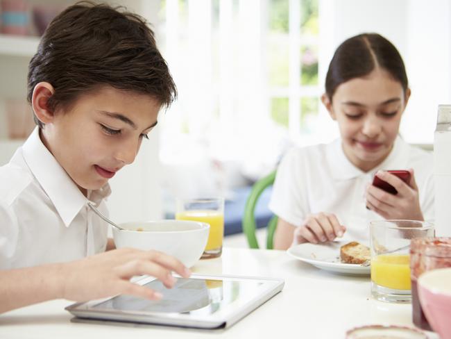 On the go ... schoolchildren with digital tablet and mobile phone at the breakfast table.