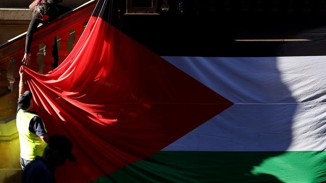 Protesters hang a large Palestinian flag on the wall of Sydney Town Hall at the start of a protest rally against Israeli military action in Gaza. Picture: David Gray/AFP