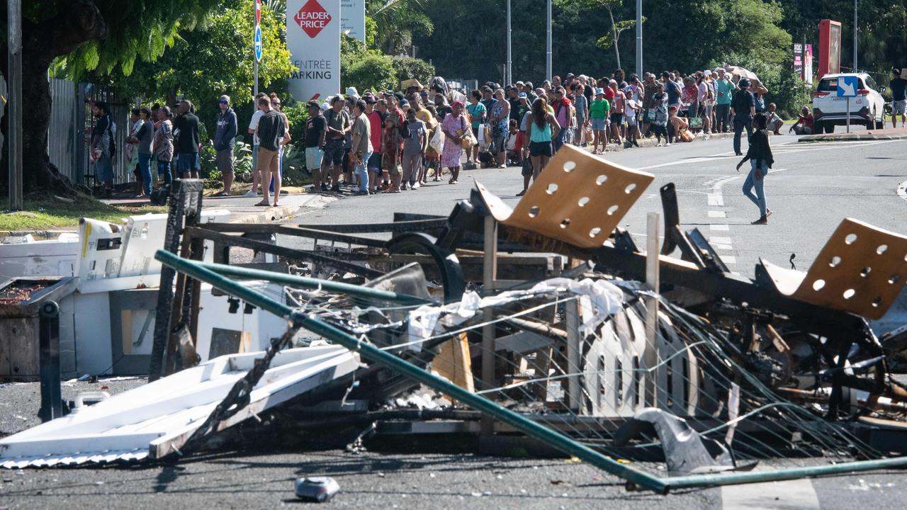 TOPSHOT - People wait in line to buy provisions from a supermarket along a street blocked by debris and burnt out items following overnight unrest in the Magenta district of Noumea, France's Pacific territory of New Caledonia, on May 18, 2024. Hundreds of French security personnel tried to restore order in the Pacific island territory of New Caledonia on May 18, after a fifth night of riots, looting and unrest. (Photo by Delphine Mayeur / AFP)