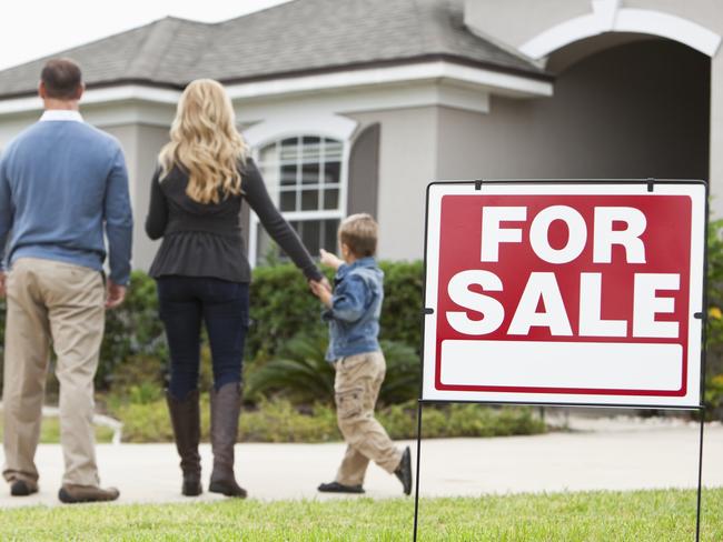 Family with two boys (4 and 6 years) standing in front of house with FOR SALE sign in front yard.  Focus on sign.