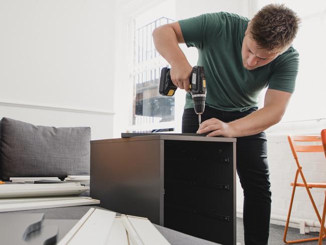 Young man putting up flat pack furniture in his new home.