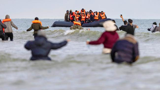 TOPSHOT - Migrants wave to a smuggler's boat in an attempt to cross the English Channel, on the beach of Gravelines, near Dunkirk, northern France on April 26, 2024. Five migrants, including a seven-year-old girl, died on April 23, 2024 trying to cross the Channel from France to Britain, local authorities said, just hours after Britain passed a controversial bill to deport asylum seekers to Rwanda. (Photo by Sameer Al-DOUMY / AFP)