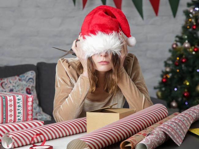 Depressed frustrated woman wrapping Christmas gift boxes, winter holiday stress concept