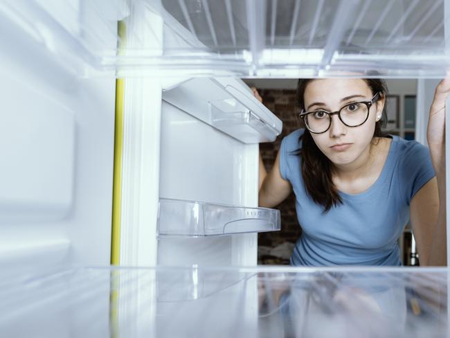 Sad woman looking into her empty fridge with no groceries; household appliances at home generic