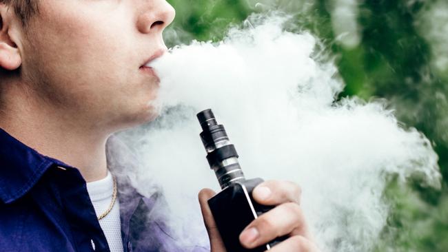 A young adult male has a cloud of nicotine vapor "smoke" pouring from his mouth.  Vape smoking, or "vaping" is growing in popularity, as well as falling under stricter state and governmental regulations.  Horizontal image with copy space.