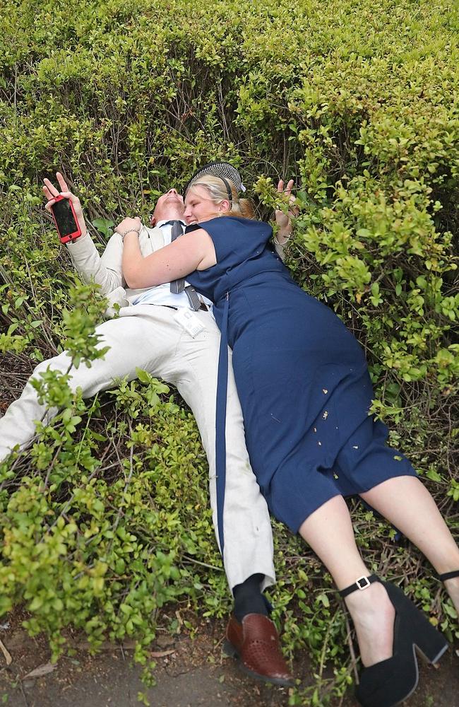 Her fascinator still firmly in place, the girl in blue with her friend lie laughing ‘in the rough’. Picture: Getty.