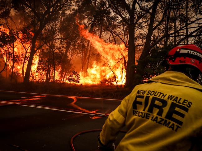 Fire and Rescue personnel run from flames as a bushfire burns trees along a road near homes on the outskirts of Bilpin, NSW. Picture: David Gray/Getty