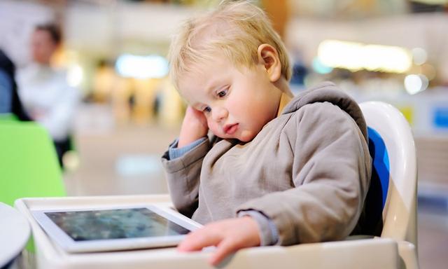 Bored blonde toddler boy with a digital tablet indoors