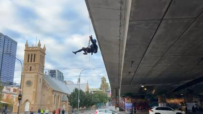 A woman hanging off a CBD bridge in as part of a protest has disrupted peak hour traffic. Picture: Facebook