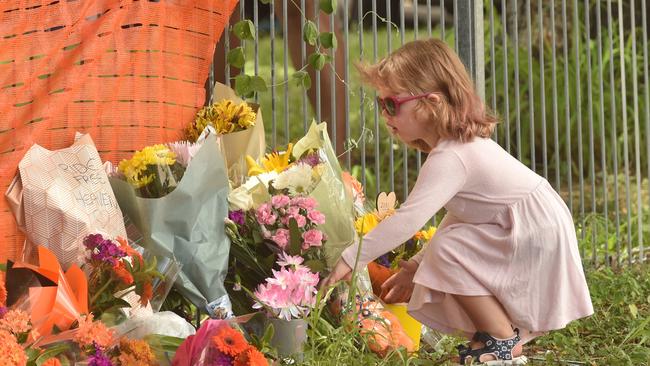 A child lays a bouquet of flowers at a memorial rally for Jennifer Board held near the accident site on Ross River Road. Picture: Evan Morgan