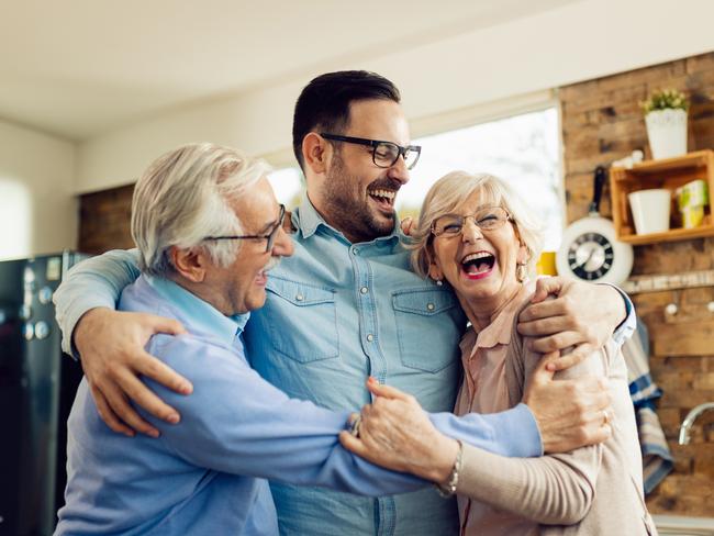 Cheerful mid adult man and his senior parents laughing while embracing in the kitchen. happy retirees generic retirement