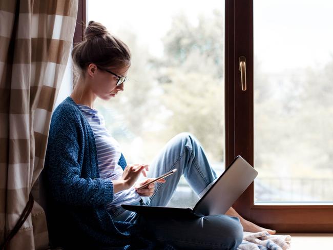 CORONAVIRUS:  Working from home. Young woman using laptop, phone, Internet. Freelancer workplace in living room office on windowsill. Distance learning, isolation, female business, shopping online. Lifestyle moment