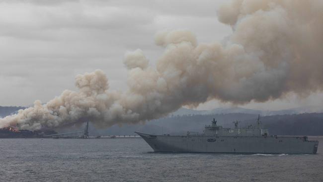 HMAS Adelaide, with the Eden timber mill burning in the background. Picture: Sean Davey
