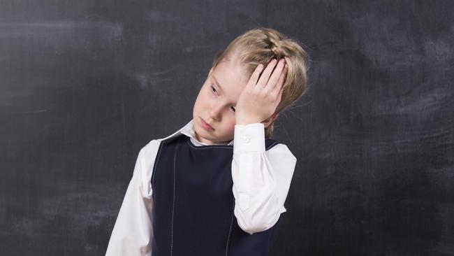 little schoolgirl with headache holding her head with hands stands at the blackboard school stress for lauren martyn jones story insight