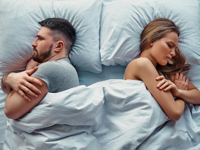 Young beautiful couple lying in bed turned back to back, arms crossed in anger and resentment. Relationship problems.Top view.