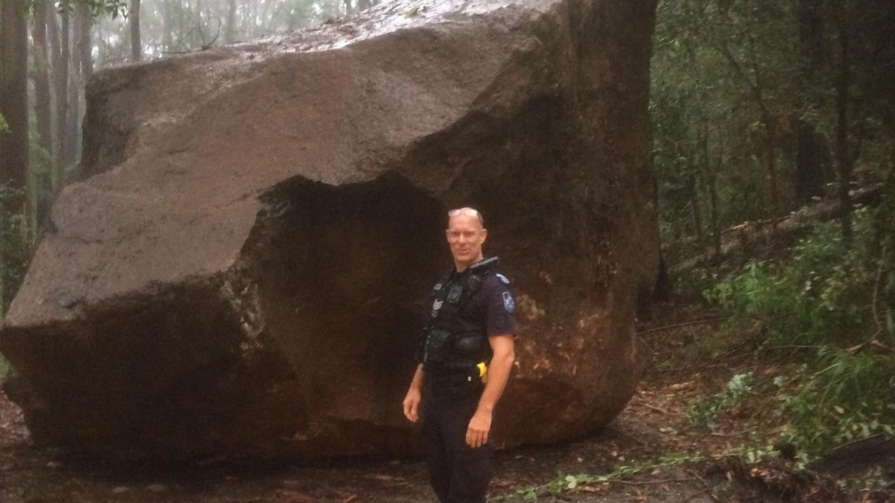 A Queensland police officer stands next to an enormous boulder in the Gold Coast hinterland following a landslide. Picture: Queensland Police