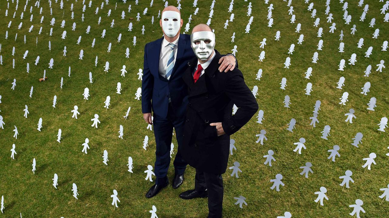Masked brothers “A”, left, and “B”, right, surrounded by paper cut outs symbolising Australia’s 1.4 million abuse victims. Picture: Tom Huntley.