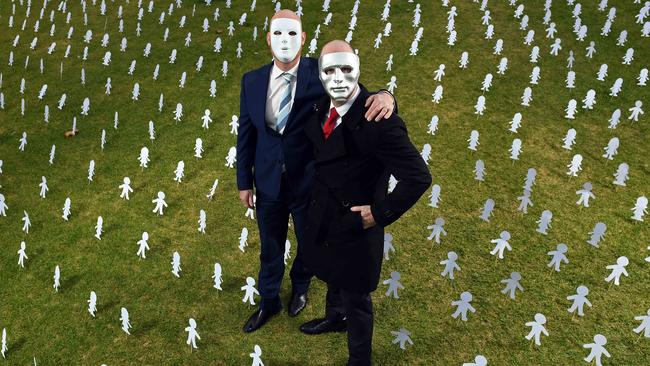 Masked brothers “A”, left, and “B”, right, surrounded by paper cut outs symbolising Australia’s 1.4 million abuse victims. Picture: Tom Huntley.