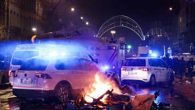 Police cars drive past burning electrical scooters