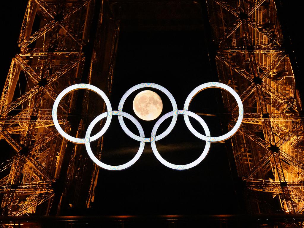 The moon rises behind the Olympic rings displayed on the Eiffel Tower in Paris.