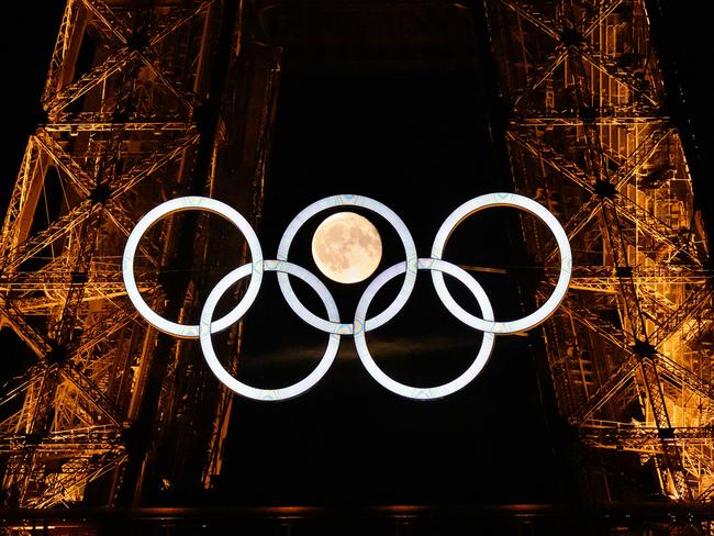 The moon rises behind the Olympic rings displayed on the Eiffel Tower in Paris.