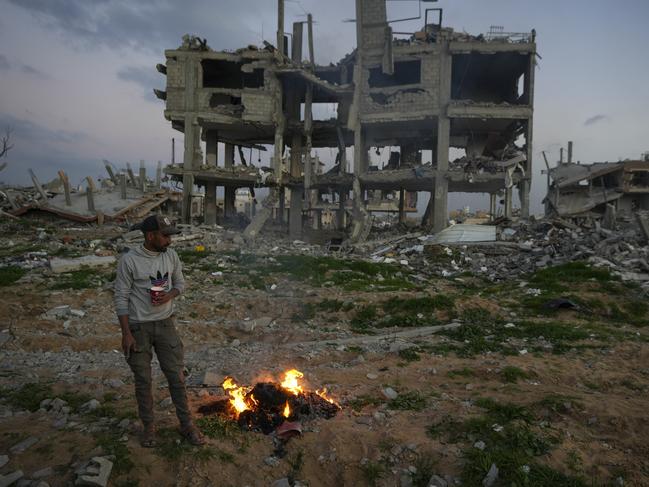 A man stands by a fire next to a destroyed house in an area littered with rubble from buildings demolished during the Israeli army's ground and air offensive against Hamas in Gaza City, Tuesday Feb. 4, 2025.(AP Photo/Abdel Kareem Hana)