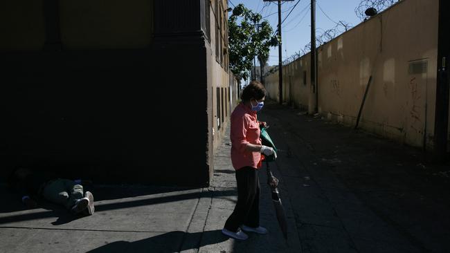 In the US, a woman with a mask and protective gloves walks past a homeless man napping on the street amid the coronavirus pandemic in the Westlake neighbourhood of Los Angeles during the week. Picture: AP