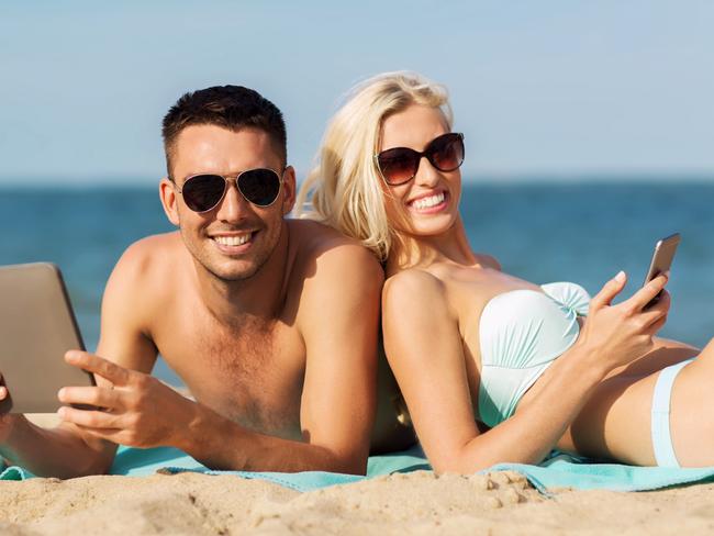 Love, travel, tourism, technology and people concept - happy couple on vacation with tablet pc computer sunbathing on summer beach Tourism Tribe