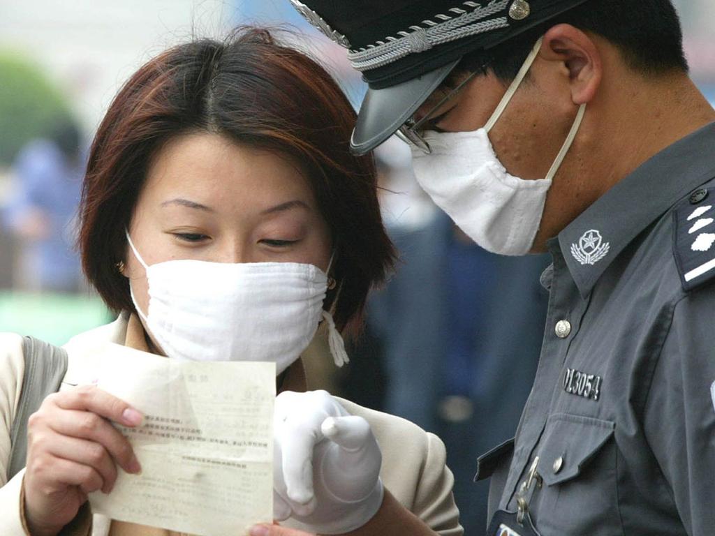 A woman fills in her health declaration in front of a police officer at Beijing Railway Station in 2003 at the height of the SARS epidemic. Picture: NewsCorp Australia.