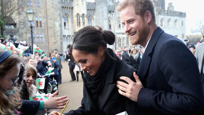 Meghan Markle writes a note for 10 year old Caitlin Clarke as Prince Harry looks on during a walkabout at Cardiff Castle in January. Picture: Getty